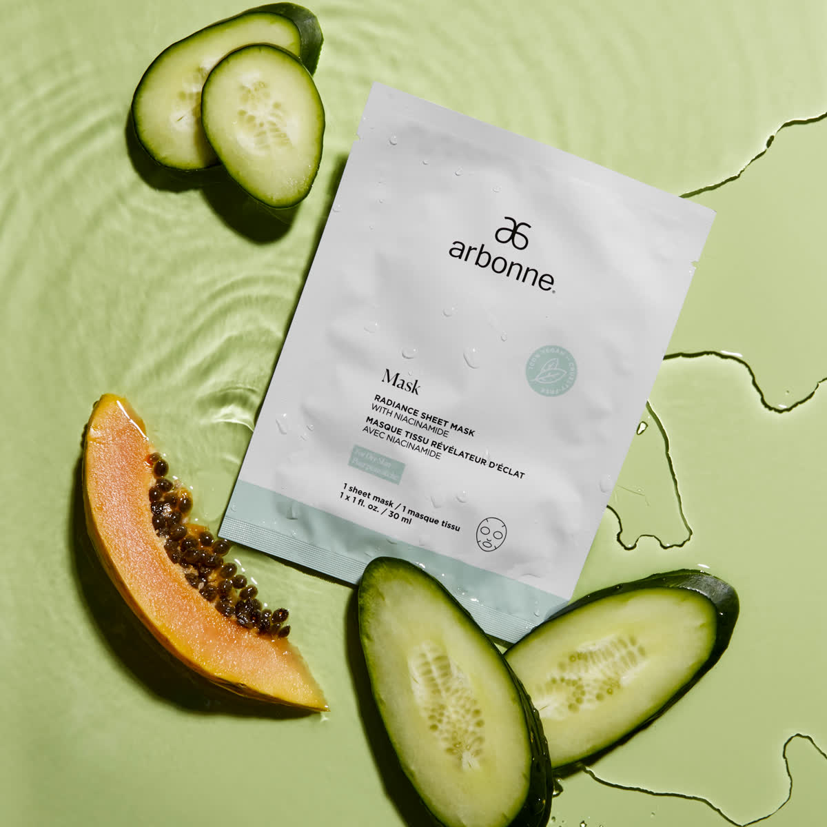 Arbonne sheet mask sachet on green with cucumber slices and papaya in water